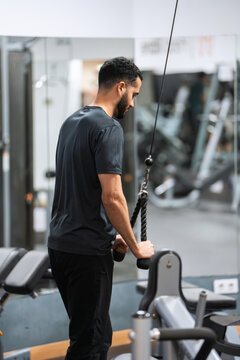 Focused gym-goer performing tricep pushdowns with a rope attachment at a fitness club. 