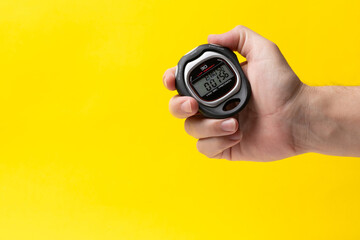 Man hand with stopwatch on a yellow background, closeup. Concept of sports.