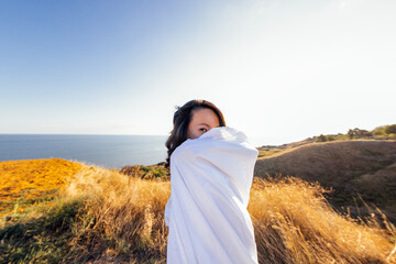 A young attractive Asian woman wrapped in a white blanket and looks at the camera and enjoys the...
