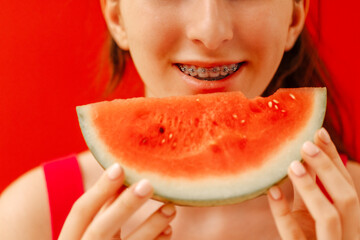 A close-up of a female teenager mouth with dental braces and a piece of delicious watermelon. The...