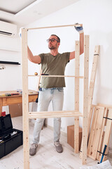 Man assembling new wooden shelf and furniture in the apartment.