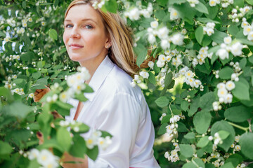 Close up of a portrait of a young beautiful blonde woman in a white shirt with jasmine flowers
