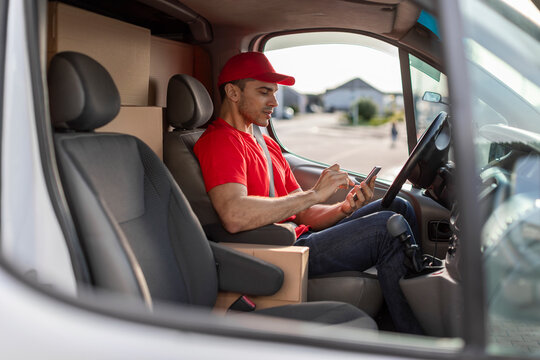 Young delivery man courier sitting in car and using mobile smartphone checking location to contact the customer for shipment