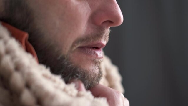 Covered with plaid bearded man freezing feeling cold at home, having fever flu influenza temperature symptoms, shivering indoors.