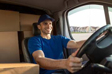 Cheerful man courier in blue uniform on driver's seat of van, delivering parcels, driving car and...
