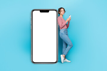 Full size photo of intelligent woman wear pink cardigan hold smartphone standing near touchscreen isolated on teal color background