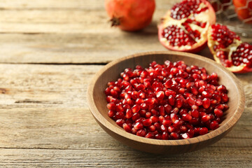 Ripe juicy pomegranate grains in bowl on wooden table. Space for text