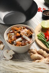 Different products and wok on light wooden table, closeup