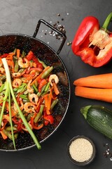 Shrimp stir fry with vegetables in wok and ingredients on black table, flat lay