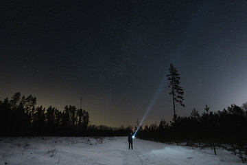 Night scene, a man with a flashlight in a winter forest under a starry sky.