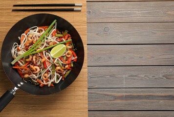 Shrimp stir fry with noodles and vegetables in wok on wooden table, top view. Space for text