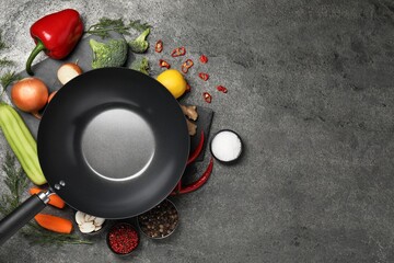 Empty iron wok surrounded by ingredients on grey table, flat lay. Space for text