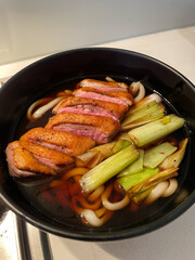 A bowl of udon soup with duck and leek.