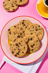 Chocolate chip cookies on a vibrant pink background with a cup of coffee.