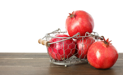 Fresh pomegranates in basket on wooden table against white background