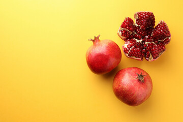 Whole and cut fresh pomegranates on yellow background, flat lay. Space for text