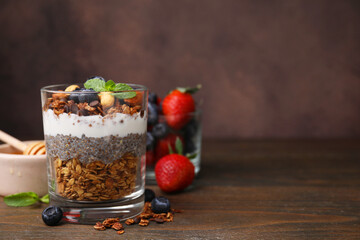 Tasty granola with berries, yogurt and chia seeds in glass on wooden table, space for text