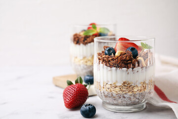 Tasty granola with berries, yogurt and chia seeds in glass on white table, space for text