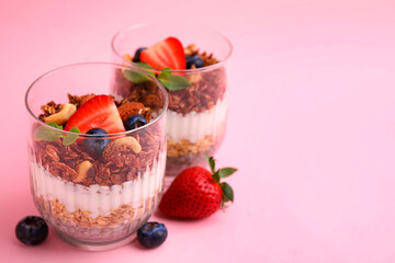 Tasty granola with berries, nuts, yogurt and chia seeds in glasses on pink background, space for text