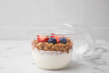 Tasty granola with berries and yogurt in plastic cup on white marble table