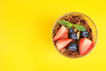 Tasty granola with berries and mint in glass on yellow background, top view. Space for text