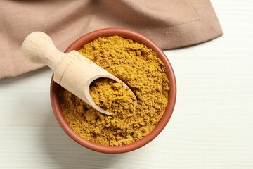 Curry powder in bowl and scoop on white wooden table, top view