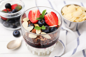 Tasty granola with berries, jam, yogurt and almond flakes in glass on white table, closeup