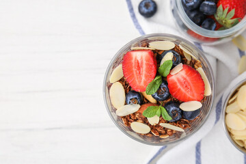 Tasty granola with berries, almond flakes and mint in glass on white table, flat lay. Space for text