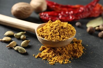 Spoon with dry curry powder and other spices on dark textured table, closeup