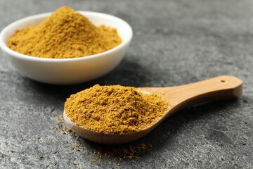 Spoon and bowl with dry curry powder on dark textured table, closeup