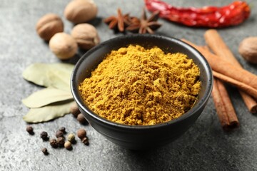 Dry curry powder in bowl and other spices on dark textured table, closeup