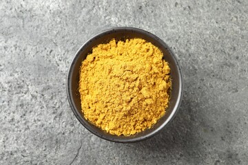 Dry curry powder in bowl on dark textured table, top view