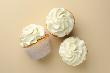 Tasty vanilla cupcakes with cream on beige background, top view