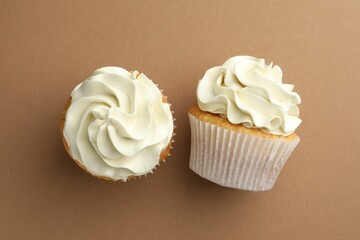 Tasty vanilla cupcakes with cream on dark beige background, top view