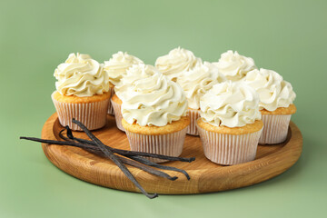 Tasty cupcakes with cream and vanilla pods on green background