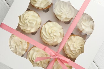 Tasty cupcakes with vanilla cream in box on white wooden table, top view