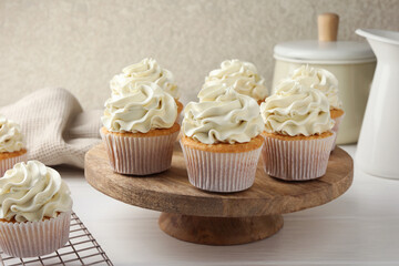 Tasty vanilla cupcakes with cream on white wooden table