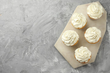 Tasty cupcakes with vanilla cream on grey table, top view. Space for text