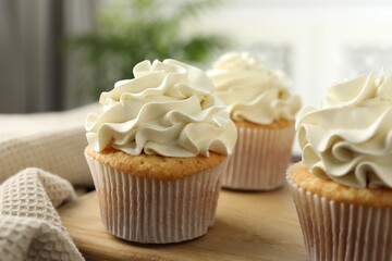 Tasty cupcakes with vanilla cream on wooden board, closeup