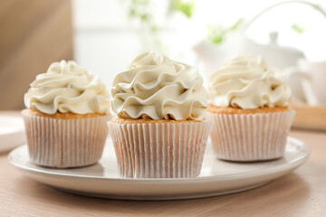 Tasty cupcakes with vanilla cream on light wooden table, closeup