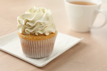 Tasty cupcake with vanilla cream on light wooden table, closeup