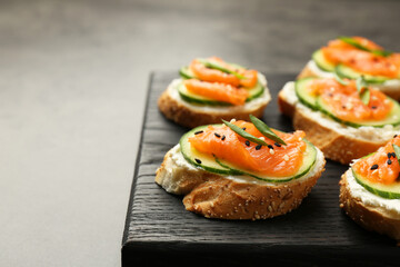 Tasty canapes with salmon, cucumber and cream cheese on grey table, closeup. Space for text