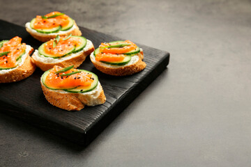 Tasty canapes with salmon, cucumber and cream cheese on grey table, closeup. Space for text