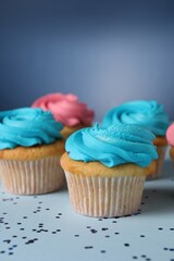 Delicious cupcakes with bright cream and confetti on blue background, closeup
