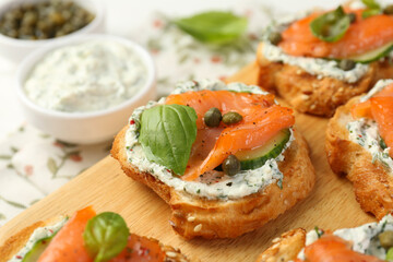 Tasty canapes with salmon, capers, cucumber and sauce on table, closeup