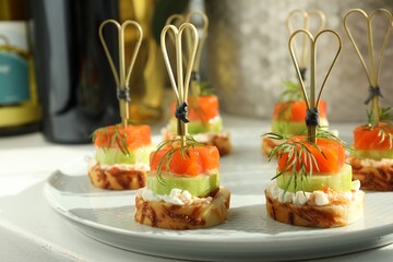 Tasty canapes with salmon, cucumber, bread and cream cheese on white table, closeup