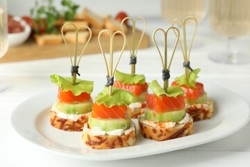 Tasty canapes with salmon, cucumber, bread and cream cheese on white wooden table, closeup