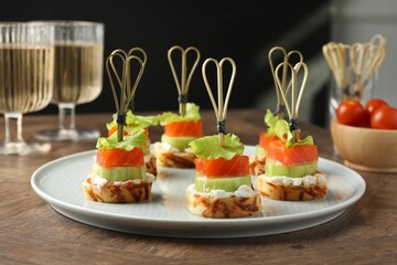 Tasty canapes with salmon, cucumber, bread and cream cheese on wooden table