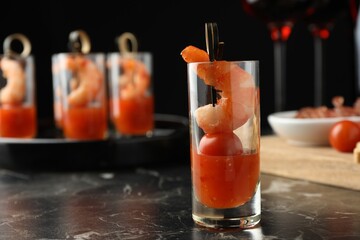Tasty canape with shrimp, tomato and sauce in shot glass on black marble table, closeup. Space for...