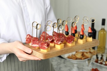 Woman holding tray of different tasty canapes indoors, closeup